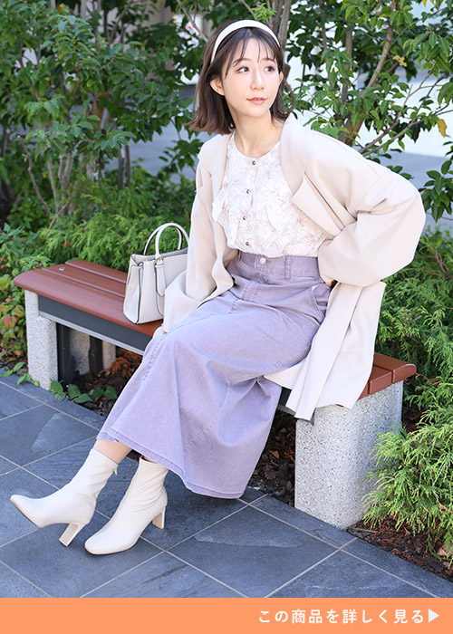 オフホワイトの花柄ブラウスとスカートのコーデにベージュのジャケットを羽織る女性