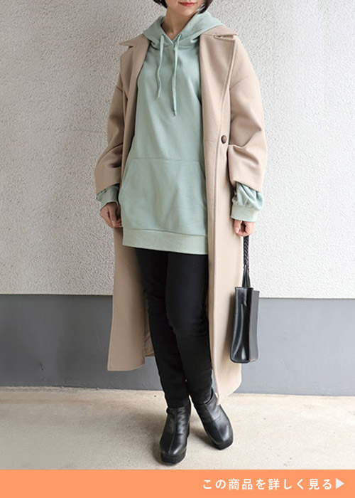 ライトグリーンのビッグパーカ×黒のスキニーパンツを着て、ベージュのロングコートを羽織る女性