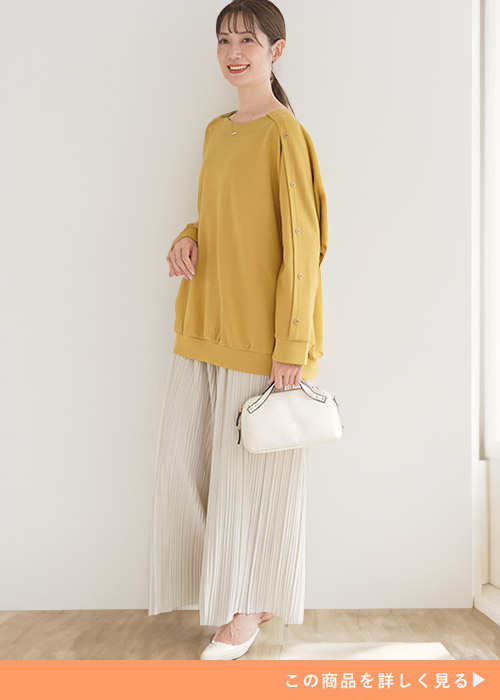マスタードカラーのトレーナー×アイボリーのプリーツパンツを着る女性