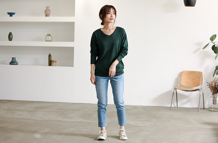 深みのあるグリーンのニットソーを着て、デニムパンツを履く女性