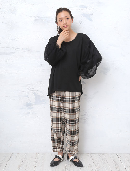 シアーなボリューム袖の黒トップスを着て、チェック柄のパンツを履く女性