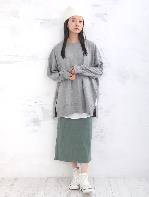 白色のトップスにグレーのニットを重ね着して、くすみカーキ色のナロースカートを履く女性