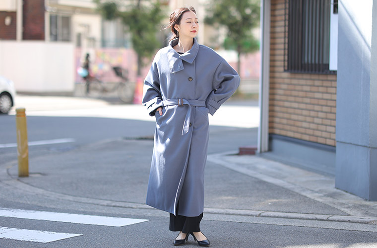 黒色のパンツを履き、スモーキーブルー色のコートを着る女性