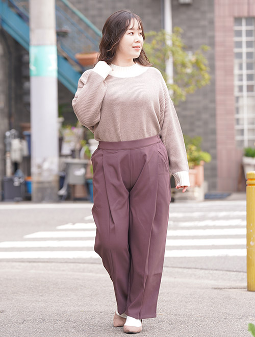 ピンクベージュのトップスを着て、ピンクブラウンのワイドパンツを履く女性