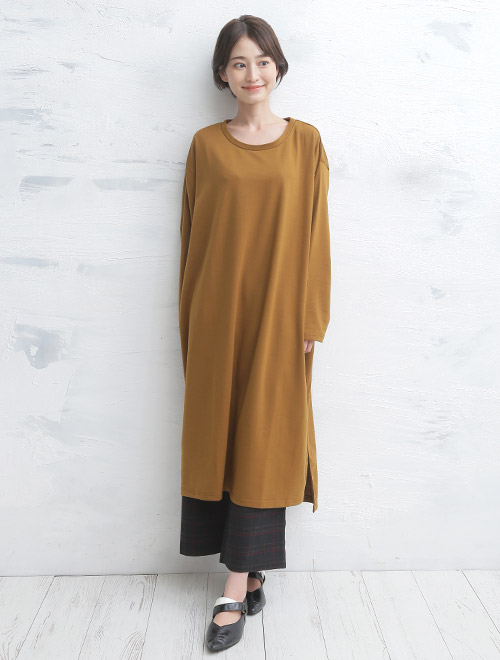 キャメル色のロングワンピースを着て、ダークな黒系のパンツを履く女性