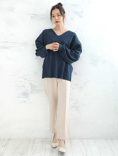 深みのある青色のVネックニットを着て、ベージュのセンターシームパンツを履く女性