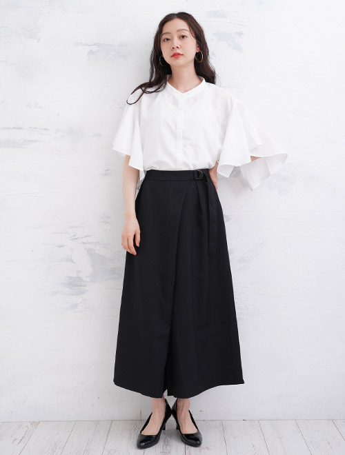 白色のフレアー袖ブラウスを、黒色のラップデザインパンツにタックインして着る女性