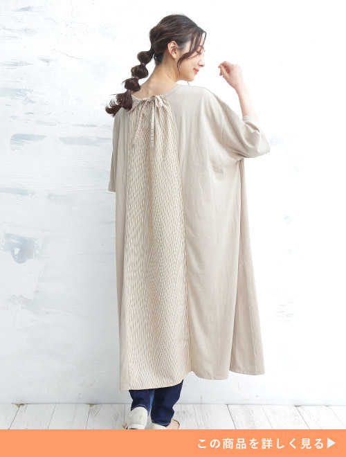 バックのセンターに縦ストライプの切り替えが入ったベージュのAラインワンピースを着る女性