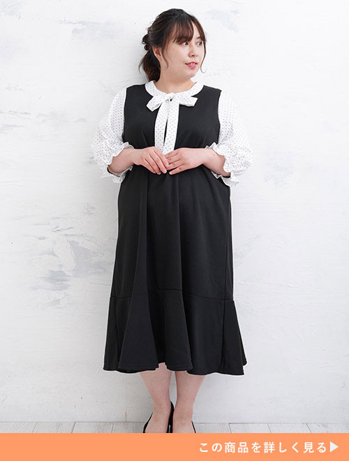 白地×黒のドット柄ボウタイブラウスを黒のノースリワンピにレイヤードしたようなマーメイドラインのドッキングワンピースを着る女性