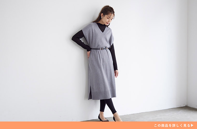 黒色のインナーとレギンスにグレーのニットベストワンピースを重ね着する女性