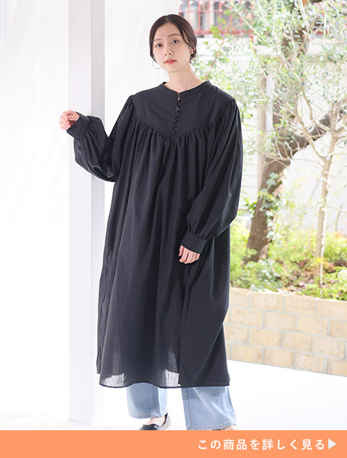 たっぷりのギャザーの入った軽やかな黒ワンピースにデニムパンツをレイヤードする女性