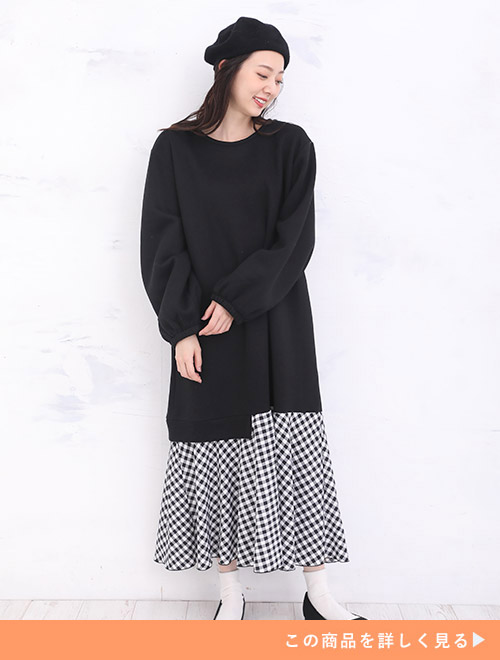 ブラックのトップスと白×黒のギンガムチェック柄スカートを合わせたようなドッキングワンピースを着る女性