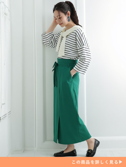ボーダートップス×グリーンのタイトスカートに、白のトップスを肩掛けする女性