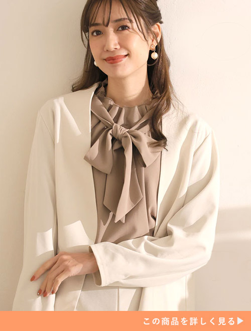 白のセットアップにベージュのリボンタイブラウスを着る女性