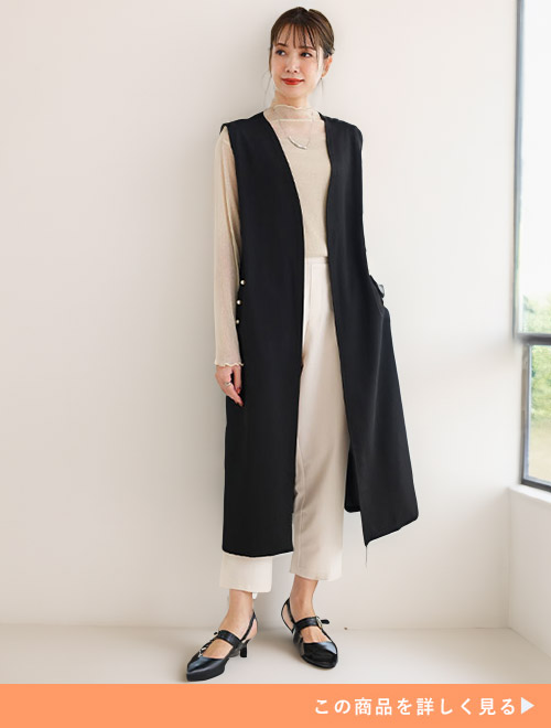 ベージュのシアートップス×パンツに、黒のジレを羽織る女性