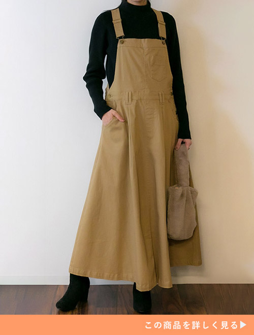 黒のタートルネックニット×ベージュのサロペスカートを着る女性