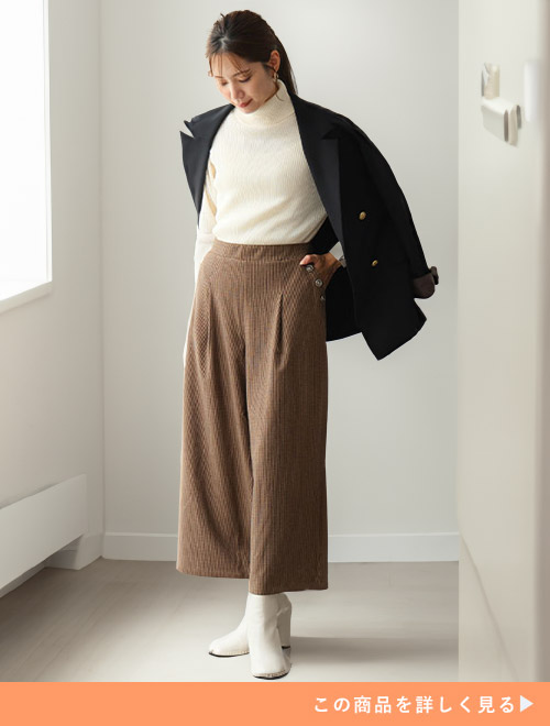 白のタートルネックニット×ブラウンのパンツに、ジャケットを肩掛けする女性