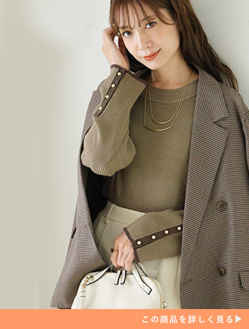 ホワイトボトムとブラウンの袖ボタンニットのコーデにジャケットを羽織る女性