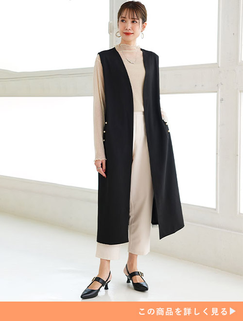 ベージュトップスとホワイトパンツのコーデに、ブラックロングジレを羽織る女性
