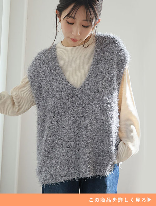 ホワイトのリブニットトップスに、ブラッシュフェザーのグレーVネックベストを羽織る女性