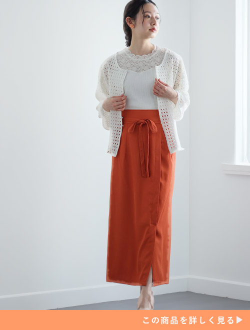アラゴンオレンジのタイトスカートとホワイトトップスのコーデに、ホワイトカーディガンを羽織る女性