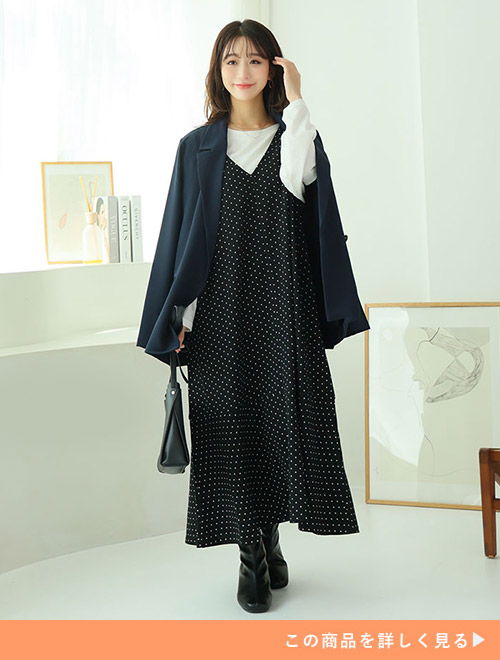 ブラックドットのジャンパースカートとホワイトトップスのコーデに、ジャケットを羽織る女性
