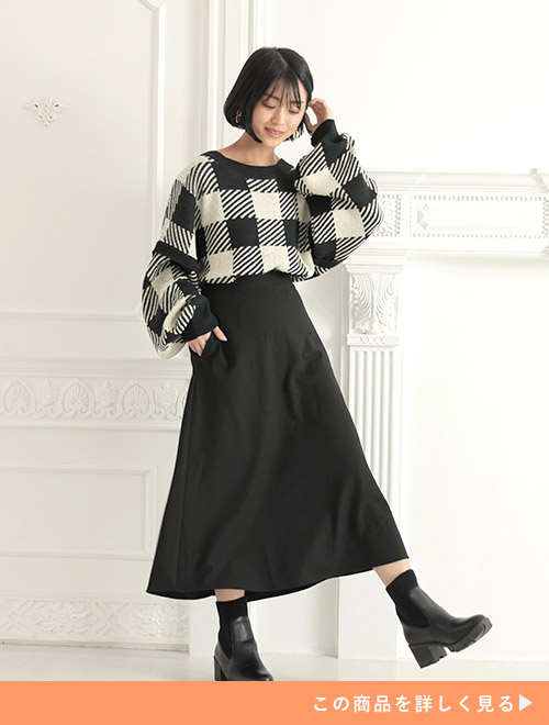 モノトーンのチェック柄トップスを着て、黒のミドル丈スカートを履く女性