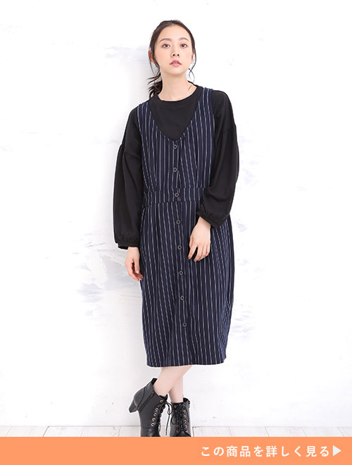 黒のトップスの上に、ミモレ丈のジャンパースカートを着た女性