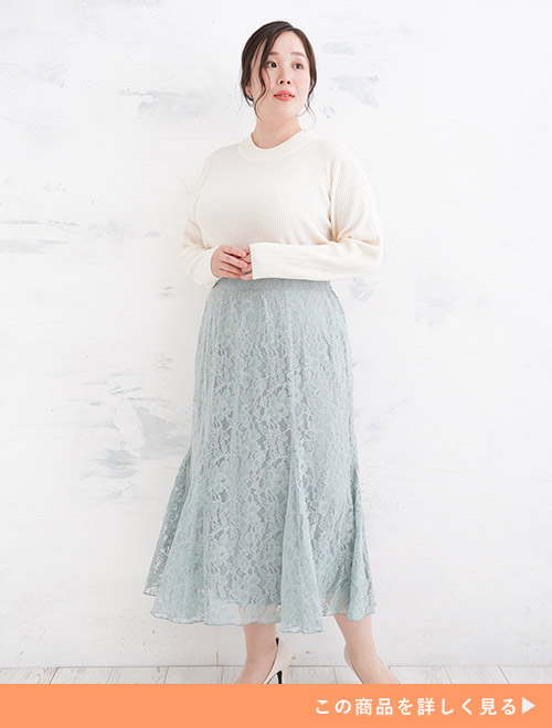 白のリブニットを着て、淡いブルーのマキシ丈レーススカートを履く女性