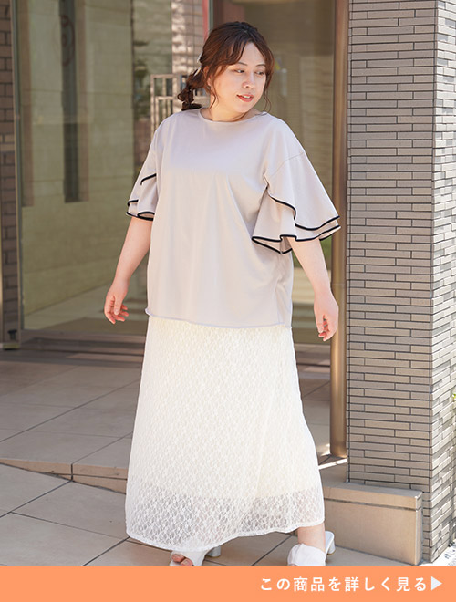 ピンクベージュの袖フリルトップスを着て、白のレーススカートを履く女性