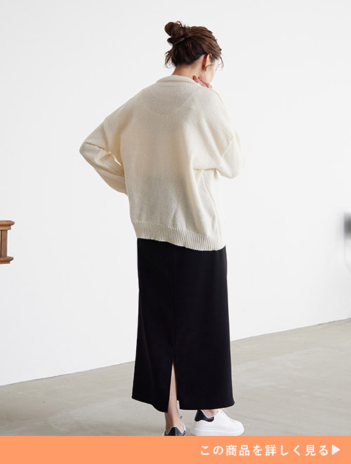 白のカーディガンを着て、黒のバックスリットスカートを履く女性