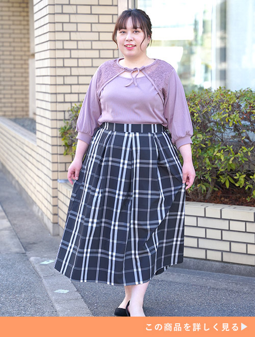 くすみパープルのトップスを着て、黒と白のチェック柄スカートを履く女性