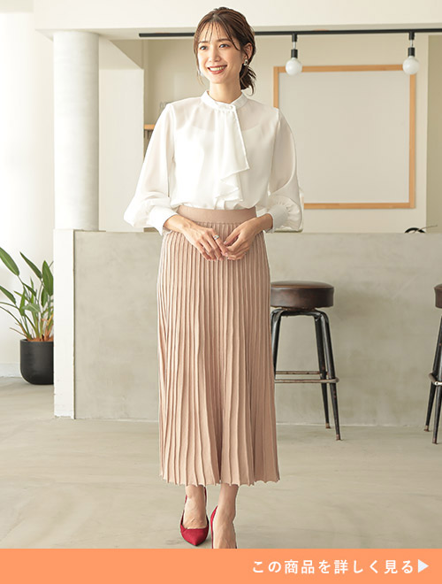 白のブラウスをインして、ベージュのプリーツスカートを履く女性