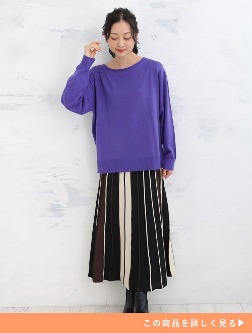 パープルのボートネックニットを着て、黒×オフホワイトのプリーツスカートを履く女性