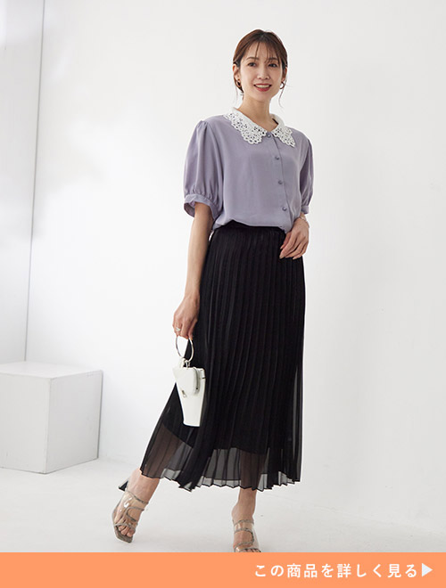 ラメシアー素材の黒のプリーツスカートに、レース襟付きのブルーのブラウスをトップスインして着る女性