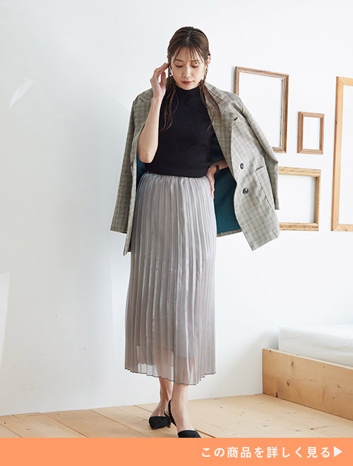 黒トップス×ラメ入りグレーのプリーツスカートコーデに、チェック柄ジャケットを肩掛けする女性