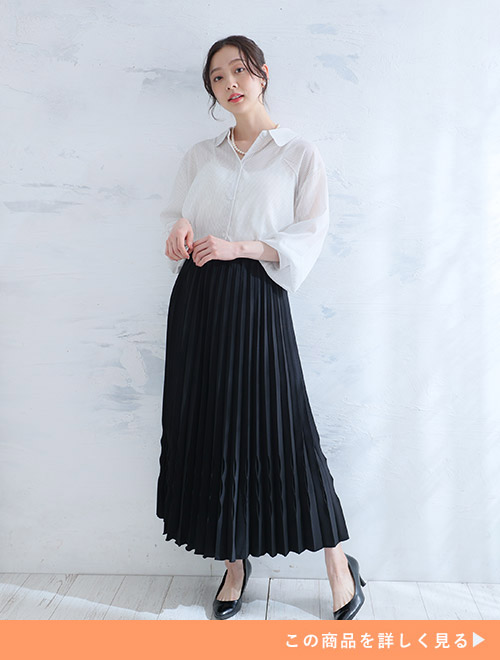 黒の変形プリーツスカートに、オフホワイトのシアーシャツをタックインして着る女性