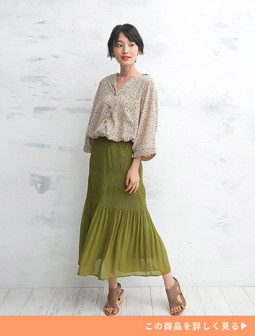 カーキの変形プリーツスカートに、ベージュ系の花柄ブラウスをタックインして着る女性