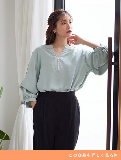 黒のパンツを履き、ミントグリーンのブラウスをタックインして着る女性