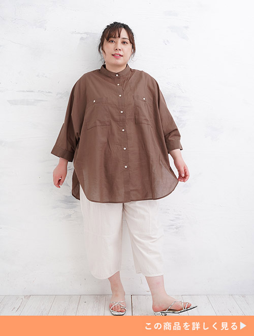 ブラウンのドルマンスリーブシャツを着て、白のクロップド丈パンツを履く女性。