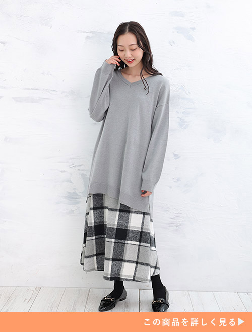 グレーのロング丈ニットを着て、ブラック系のチェック柄ロングスカートを履く女性