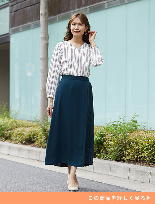 ダークグリーンのサイドプリーツスカートに、ストライプ柄のトップスをタックインして着る女性