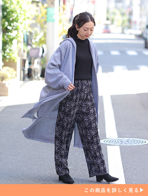 黒でまとめたトップス×花柄パンツのコーデに、グレーのロング丈フーディーを羽織る女性
