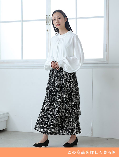 黒地のレオパード柄ロングスカートに、白のブラウスをトップスインして着る女性
