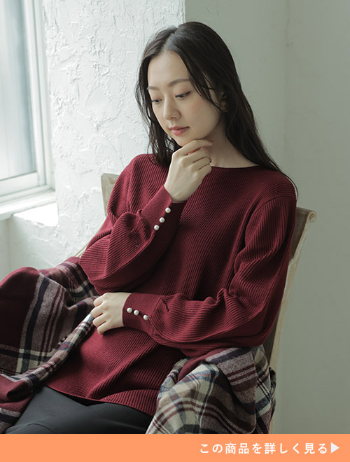 ボルドーのニット×黒スカートのコーデに、同じく赤黒配色のストールをまとう女性。