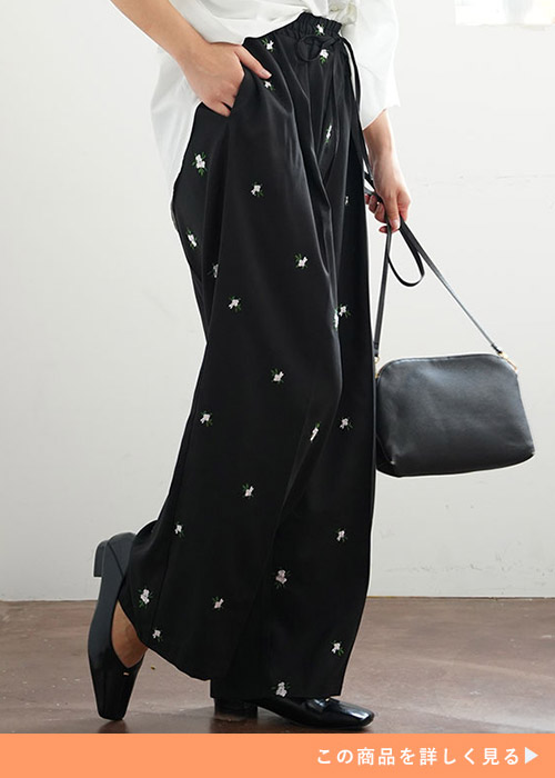 花の刺しゅう入りの黒のワイドパンツに白シャツを着る女性