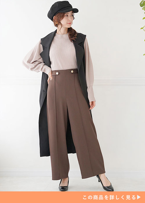 黒のチュニックブラウスを着て、ボルドーのワイドパンツを履く女性