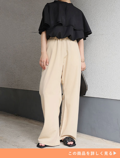 ブラックフリルトップスとエクリュの美脚カーゴパンツにブラックバッグとミュールを合わせる女性