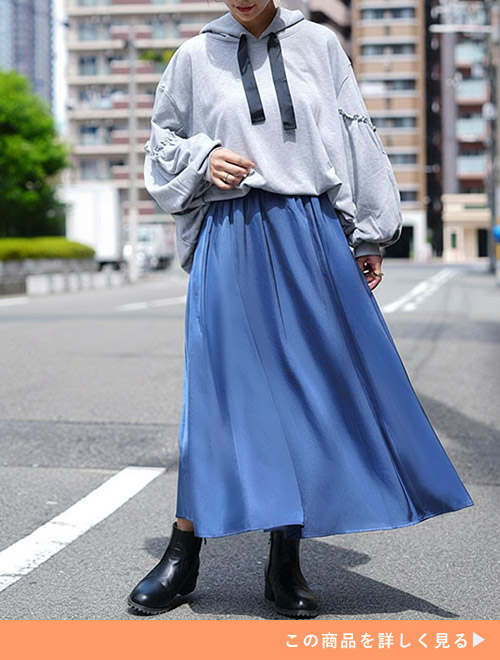 ボリューム袖のパーカにスモーキーブルーのサテンフレアスカートを履く女性