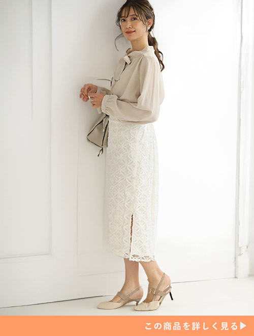 ベージュのリボンブラウスとホワイトのタイトスカートのコーデにベージュパンプスを合わせる女性